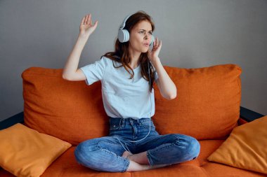 Güzel bir kadın turuncu kanepede oturmuş kulaklıklarla müzik dinliyor.