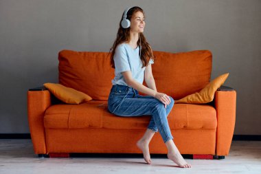 Turuncu koltukta oturmuş kulaklık teknolojisiyle müzik dinleyen güzel bir kadın.