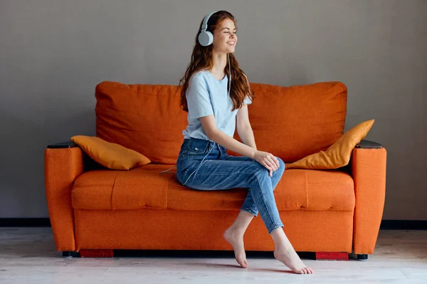 Belle femme sur le canapé orange écouter de la musique avec des technologies casque — Photo