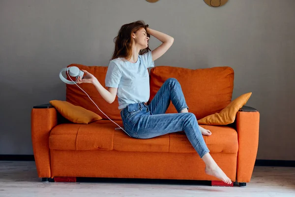 Mujer sonriente en el sofá naranja escuchando música con tecnología de auriculares — Foto de Stock