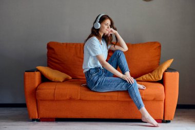 Turuncu koltukta oturan kadın kulaklık teknolojisiyle müzik dinliyor.