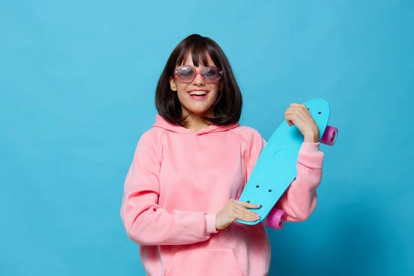 Kvinna i solglasögon med en skateboard blå bakgrund — Stockfoto