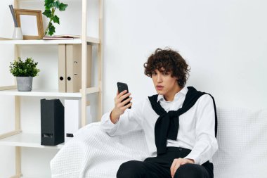Beyaz koltukta oturan adam akıllı telefon oturma odasında.