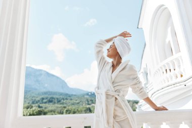 Beyaz cüppeli kadın yeşil doğa dağ manzaralı balkonda.