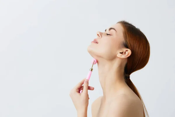 Young woman pink quartz roller skin care massage bare shoulders light background — Stock Photo, Image