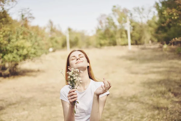 Donna con fiori bianchi in mano sta riposando nel campo e alberi Sullo sfondo — Foto Stock