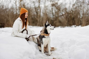 Karda genç bir kadın köpekle oynuyor. Eğlenceli bir arkadaşlık havası.