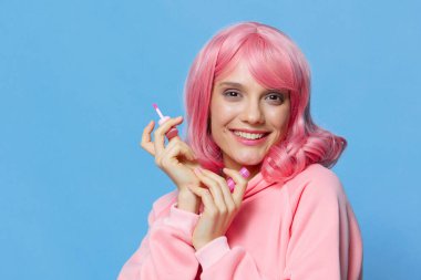 Pembe saçlı, makyajlı, mavi arka planlı bir portre kadını.