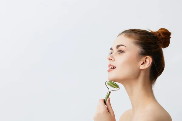 Pretty woman jade face massager wrinkle smoothing light background — Stock Photo, Image