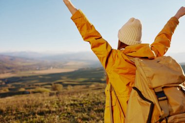 Sırt çantalı sarı ceketli bir kadın turist dağları geziyor.