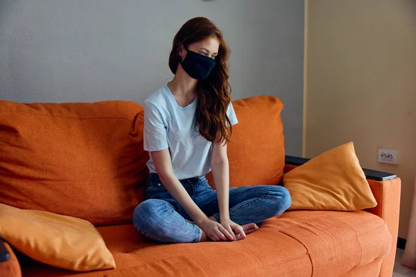 Ritratto di una donna che indossa una maschera si siede su un divano arancione a casa Stile di vita — Foto Stock