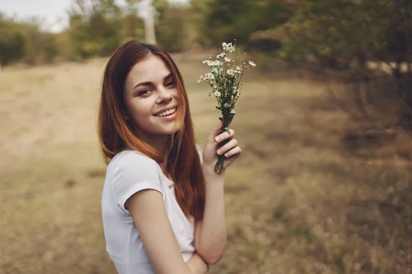 Tarlada ağaçların yanında bir buket kır çiçeğiyle romantik bir kadın — Stok fotoğraf