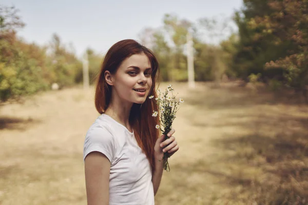 Donna con fiori bianchi in mano sta riposando nel campo e alberi Sullo sfondo — Foto Stock