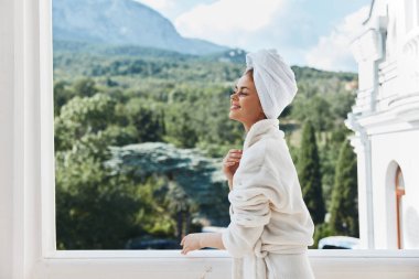 Güzel bir kadın balkonda durmuş dağlara bakıyor yazın dağlarda değişmeden tatil yapıyor.