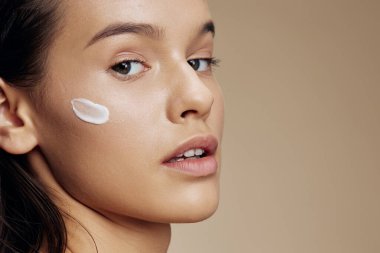 Güzel kadın cilt bakımı için yüz bej arka planda beyaz maske kullanılıyor.