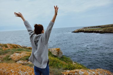 Gri kazaklı güzel kadın kayalık bir sahil manzarası üzerinde duruyor. Rahatlama kavramı.