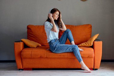 Turuncu koltukta kulaklıkla müzik dinleyen gülümseyen bir kadın.