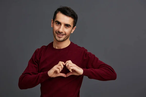 Bello uomo posa sorriso gesto mani rosso maglione grigio sfondo — Foto Stock