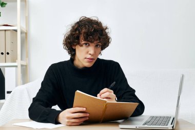 Dizüstü bilgisayarın önündeki beyaz koltukta oturan kıvırcık çocuk.