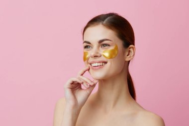 Güzel kadın altın yamalar, temiz ten tebessümü pembe arka plan pozu.