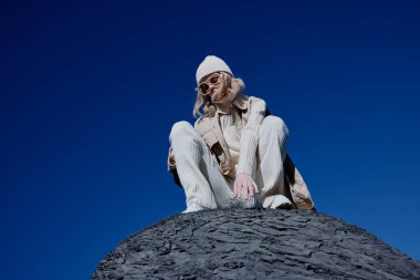 Taştan bir doğa üzerinde oturan turist şapka takan mavi gökyüzü