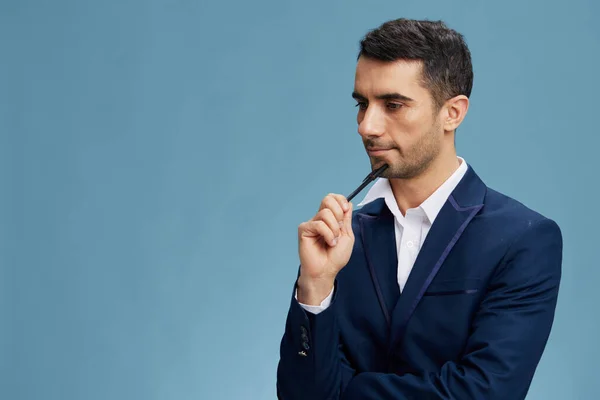 Jóképű üzletember toll a kezében egy elegáns öltöny pózol önbizalom kék háttér — Stock Fotó