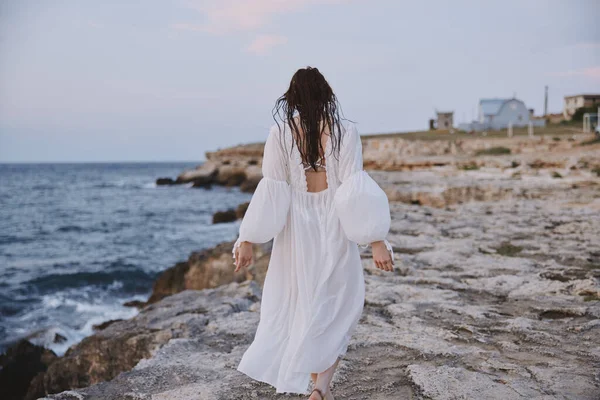 Taş plajda beyaz elbiseli bir kadın yürüyor. — Stok fotoğraf