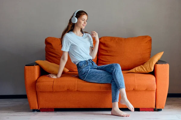 Bela mulher sentada no sofá em casa ouvindo música em fones de ouvido apartamentos — Fotografia de Stock