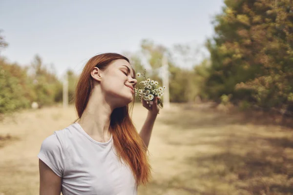 Mulher com flores brancas na mão está descansando no campo e árvores No fundo — Fotografia de Stock