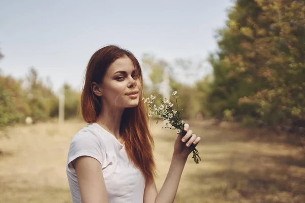 Donna con fiori bianchi in mano sta riposando nel campo e alberi Sullo sfondo — Foto Stock