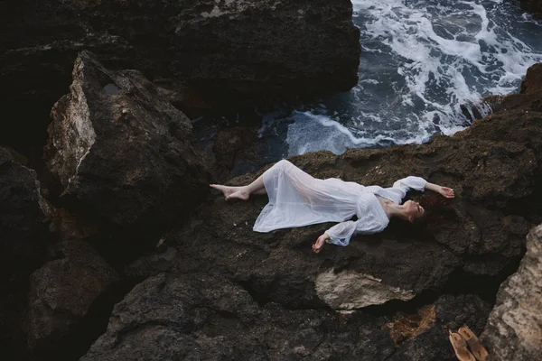 赤脚女人躺在岩石海岸上 岩石表面的地貌上有裂缝 高质量的照片 — 图库照片