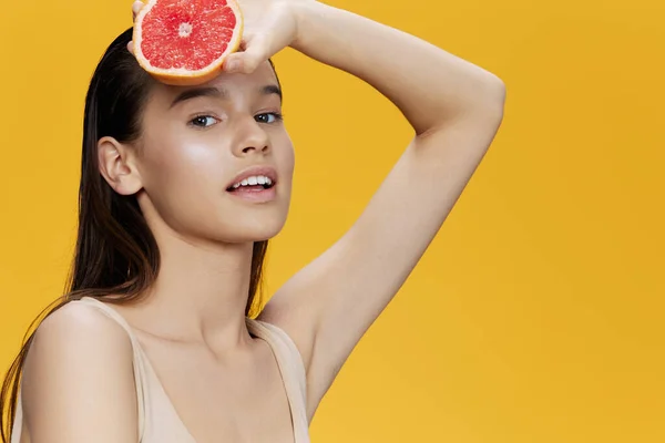 Brunette half a grapefruit vitamins health cosmetology yellow background — Stock Photo, Image