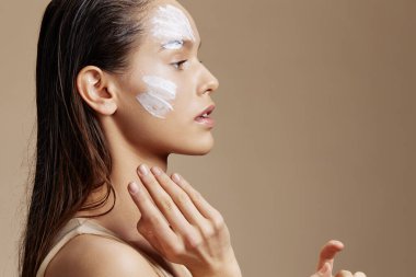 Genç bir kadının cilt bakımı için yüzü beyaz maske ile izole edilmiş.