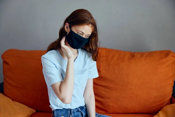 Ritratto di una donna in nero maschere mediche isolamento a casa sul divano rimanere a casa concetto — Foto Stock