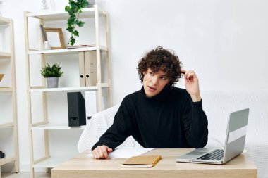 Dizüstü bilgisayarın önündeki beyaz koltukta oturan adam oturma odasını öğreniyor.