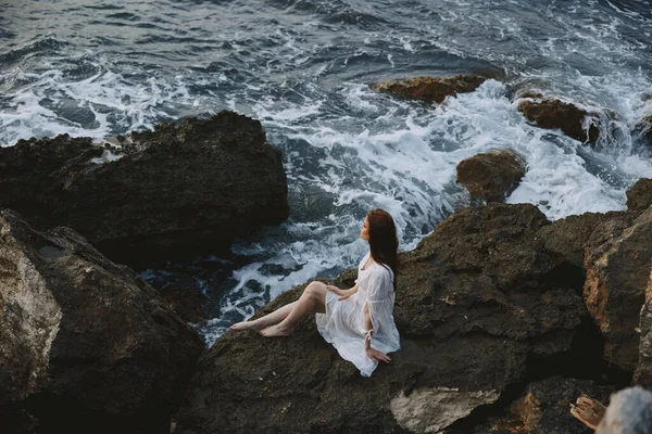 Donna scalza in un abito da sposa sulla scogliera onde tempo nuvoloso — Foto Stock