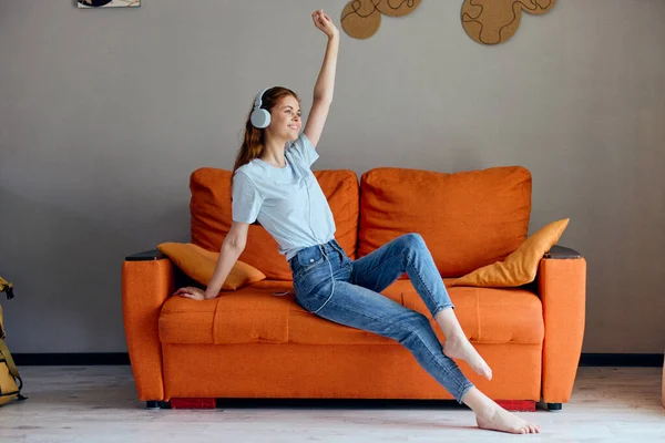 Mujer bonita sentada en el sofá en casa escuchando música en auriculares sin alterar —  Fotos de Stock