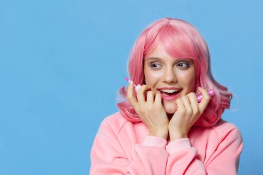 Pembe saçlı, makyajlı, mavi arka planlı bir portre kadını.