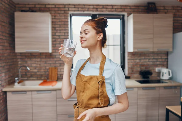 Mujer alegre beber agua en un delantal marrón cocina interior hogar vida — Foto de Stock