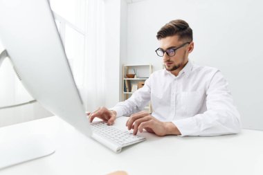 Beyaz tişörtlü işadamları telefon ofisi olan bir bilgisayarın başında otururlar.