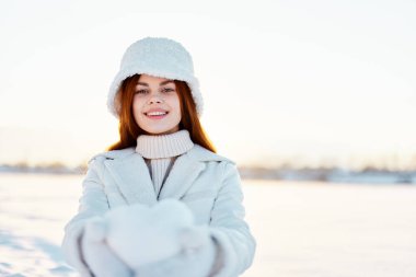 Kadın gülümse kış havasında yürü beyaz ceketli, elinde kar var.