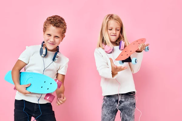 Elegante bambino e ragazza carina in cuffie skateboard in mani sfondo di colore rosa — Foto Stock