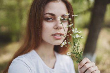 Beyaz kır çiçekleri olan güzel bir kadın açık arazide tişört giymiş.