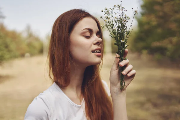 Donna romantica con un mazzo di fiori selvatici vicino agli alberi in un campo nella natura — Foto Stock