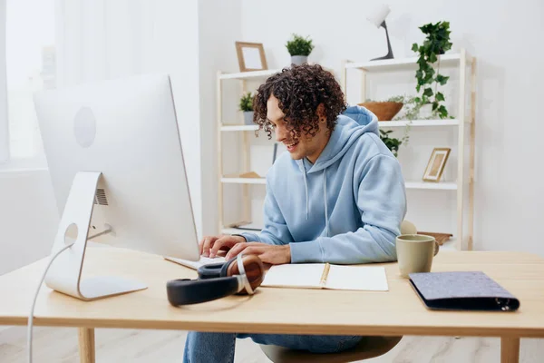 Kıvırcık saçlı bir adam bilgisayar teknolojisinin önünde masada oturuyor. — Stok fotoğraf