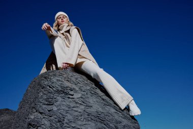 Sonbahar giysileri içinde bir kadın bir kayanın üzerinde duruyor mavi gökyüzü yaşam tarzı