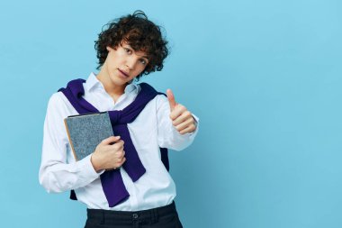Omuzlarında süveter tişörtü olan mavi arka planda not defteri olan öğrenci.