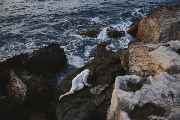 長い白いドレスの美しい花嫁濡れた髪は上から岩の崖の景色に横たわっています — ストック写真
