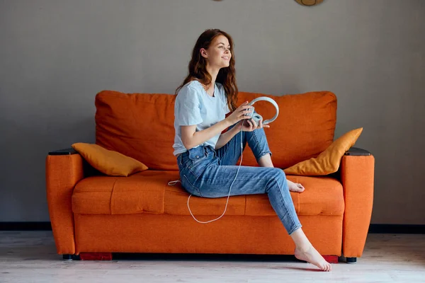 Evdeki koltukta oturmuş kulaklık teknolojisiyle müzik dinleyen bir kadının portresi. — Stok fotoğraf