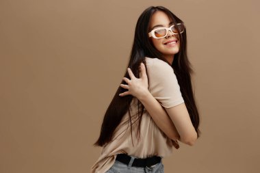 Gözlüklü, bej renkli tişörtlü, güzel bir kadın. Giyim tarzı bej arka plan.